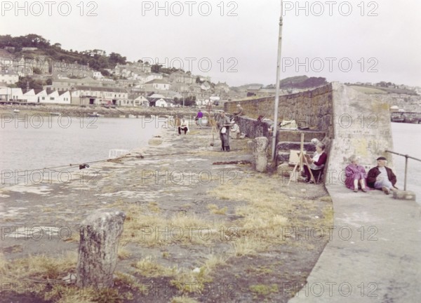 Artists painting on the sea wall in the harbour pf fishing village, Newlyn, Cornwall, England, UK c 1960