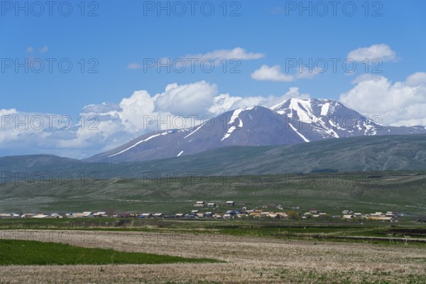 View of snow-capped mountains behind vast fields and a village, landscape near Satche, Mount Didi Abuli, Samtske-Javakheti region, Samtske Javacheti, Lesser Caucasus, Georgia
