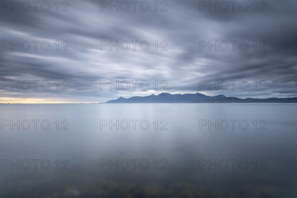 The Vestfjord in Nordland, Norway, near Bodø, impresses with a dramatic atmosphere. Dark clouds sweep across the water and create a mystical atmosphere. The rugged cliffs and majestic mountains are reflected in the tranquil fjord and provide an impressive backdrop