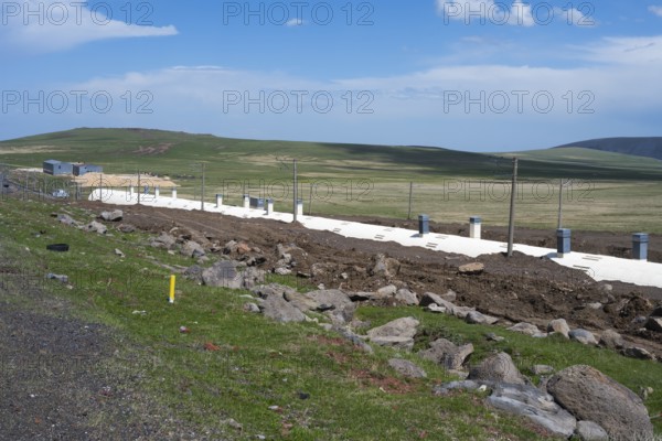 Wide landscape with green field and blue sky, in the foreground a road and a covered railway track, partly covered railway line on Lake Parawani, in the highlands of Samtskhe—Javakheti, Samtskhe-Javakheti, Lesser Caucasus, Georgia