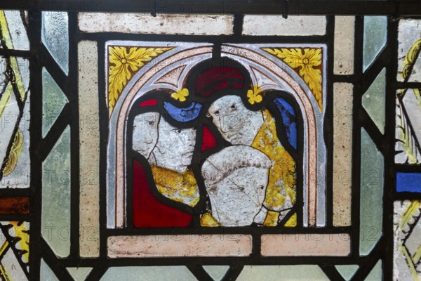 Close-up of medieval style stained glass showing faces of people, Ufford church, Suffolk, England, UK