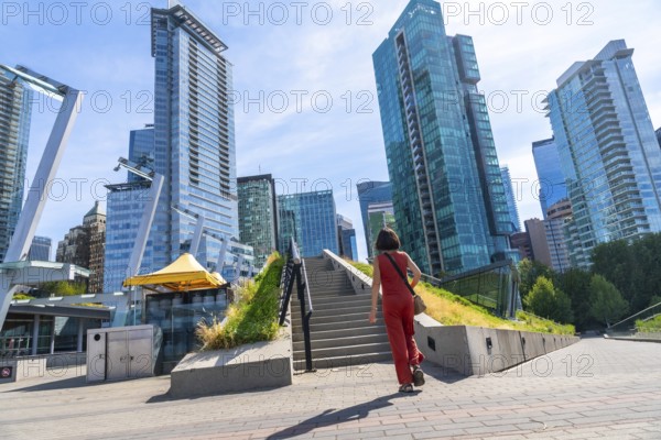 Tourist walking up stairs in downtown vancouver with modern skyscrapers, green roof and blue sky in the background, british columbia, canada