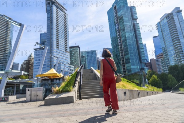 Young woman tourist walking up stairs in a modern city park with skyscrapers and office buildings in the background in vancouver, british columbia