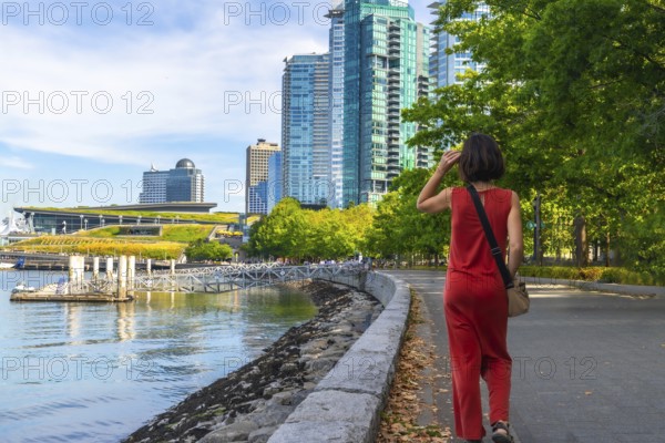 Tourist walking along the scenic seawall in vancouver, enjoying the sunny summer day while surrounded by the impressive convention center and modern skyscrapers in the background