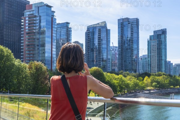 Tourist is making a phone call while enjoying the view of the modern buildings of vancouver's skyline from the cambie street bridge on a beautiful sunny day