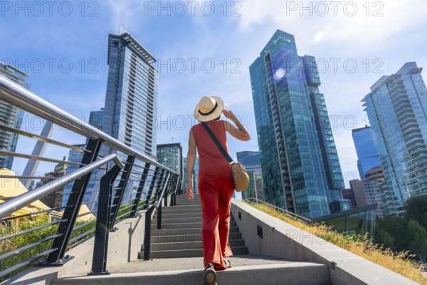 Tourist wearing a straw hat walking up stairs in vancouver, british columbia, canada with modern buildings and blue sky in background during sunny summer day