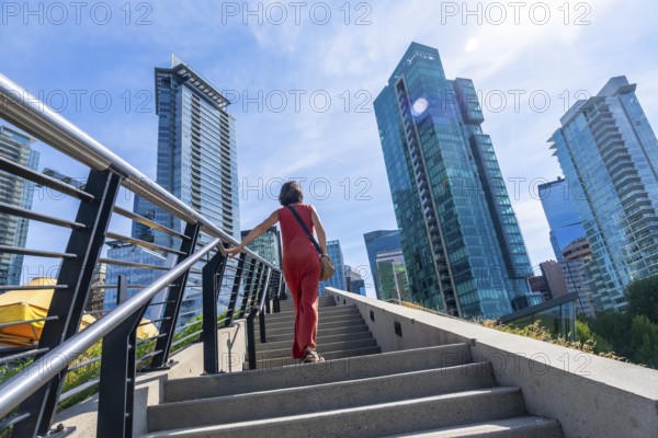Tourist walking up stairs with skyscrapers and modern architecture in the background, enjoying a sunny summer day in vancouver, british columbia, canada