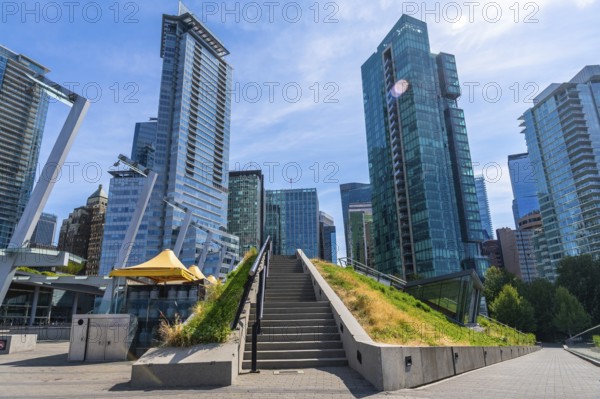 Stairs leading up a grassy knoll with modern skyscrapers towering above in the heart of vancouver, british columbia, showcasing a blend of urban development and green spaces