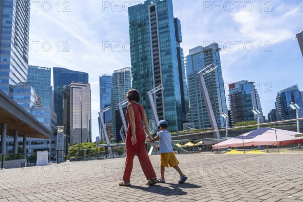 Mother and son holding hands walking in downtown vancouver, british columbia, canada, enjoying a sunny summer day surrounded by modern skyscrapers