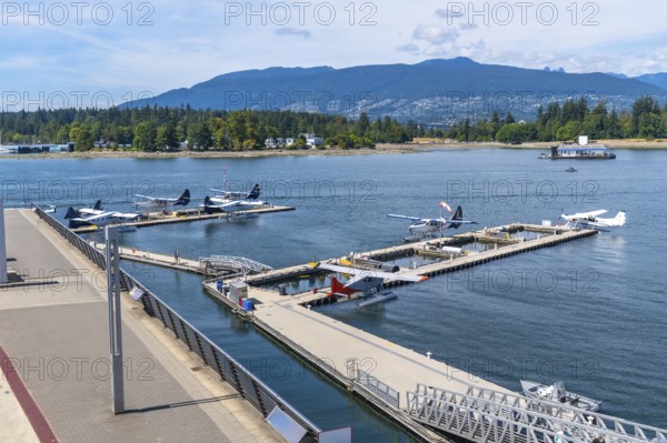 Seaplanes are docked in the harbor at coal harbour in vancouver, british columbia, canada, with stanley park and the north shore mountains in the background on a sunny summer day