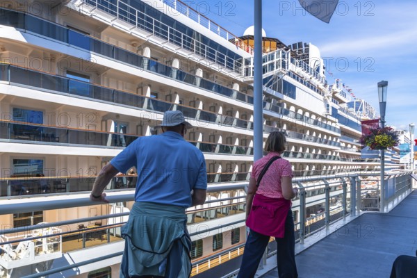 Two tourists are enjoying the view of a large cruise ship docked at canada place in vancouver, british columbia, contemplating the beginning of their maritime adventure