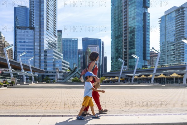 Mother and son enjoying a leisurely stroll through a modern urban square, surrounded by the impressive glass skyscrapers of downtown vancouver, british columbia, on a sunny day