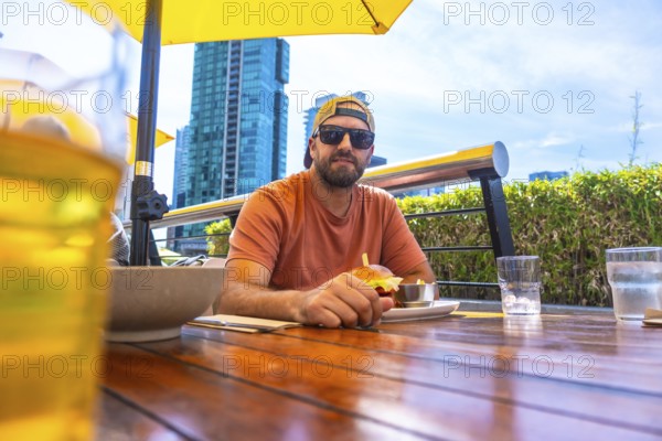 Tourist is having a burger and beer at an outdoor restaurant in vancouver, british columbia, with modern buildings in the background on a sunny day