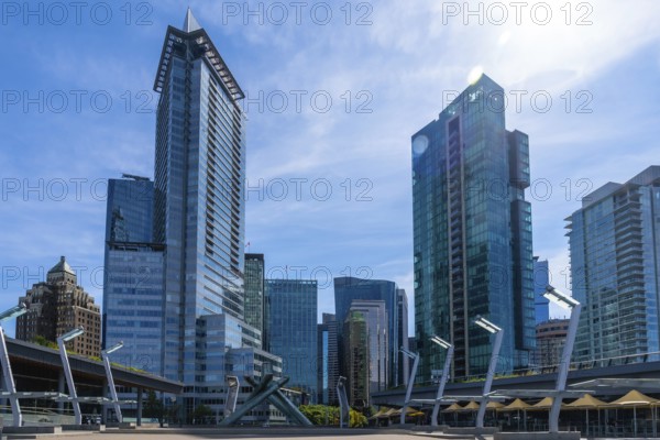 Sunlight illuminates modern skyscrapers and office buildings in vancouver, british columbia, creating a dynamic cityscape against a vibrant blue sky