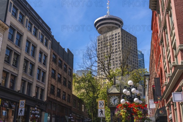 Gastown steam clock with flower decorations rising towards harbour centre, a skyscraper located in downtown vancouver, british columbia, canada, on a beautiful summer day