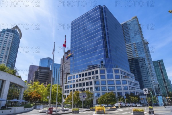 Modern skyscrapers rising against a blue sky, with canadian and pride flags waving in the foreground, symbolizing inclusivity and diversity in vancouver's urban landscape