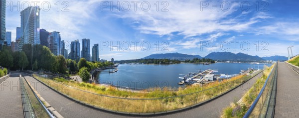 Panoramic view of vancouver's modern skyline rising above a picturesque waterfront, showcasing lush parks, calm blue waters, and boats swaying on a sunny day