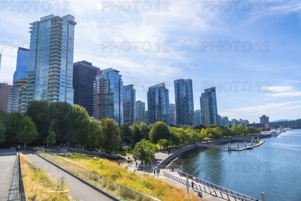 Vancouver's modern cityscape rises above a vibrant waterfront park, showcasing a blend of urban development and natural beauty on a clear, sunny day