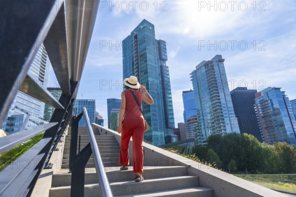 Young woman with hat and orange jumpsuit climbing stairs in vancouver downtown with modern skyscrapers and blue sky in background on a sunny summer day