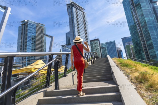 Female tourist wearing a straw hat and red jumpsuit walking up stairs in downtown vancouver, british columbia, canada, admiring the modern architecture
