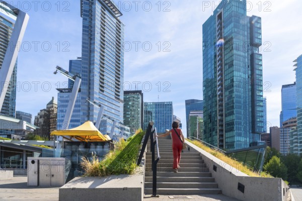 Businesswoman climbing stairs in a green urban space with skyscrapers in the background in vancouver, british columbia, enjoying modern architecture and a sunny day