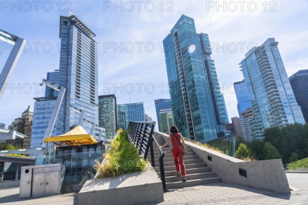 Woman is climbing the stairs of a pedestrian overpass with modern skyscrapers and a clear blue sky in the background in vancouver, canada