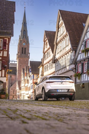 White Renault car in an old town with half-timbered houses and church tower in the background, Deer e-Carsharing, Renault Megane, Calw, Germany