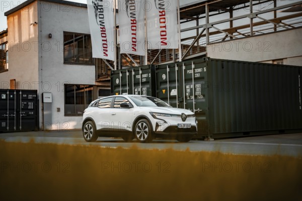 White modern SUV in front of an industrial building with containers and banners, Deer E-Carsharing, Renault Megane, Calw, Germany