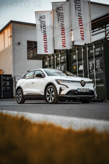 White electric car in front of a Motorworld building with flags and containers, Deer e-Carsharing, Renault Megane, Calw, Germany
