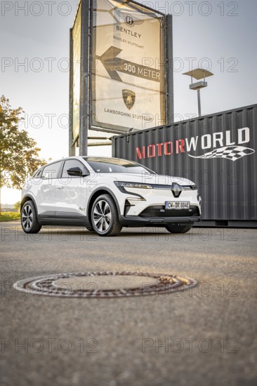 A white electric car is parked in front of a Motorworld sign on a sidewalk, Deer E- Carsharing, Renault Megane, Calw, Germany