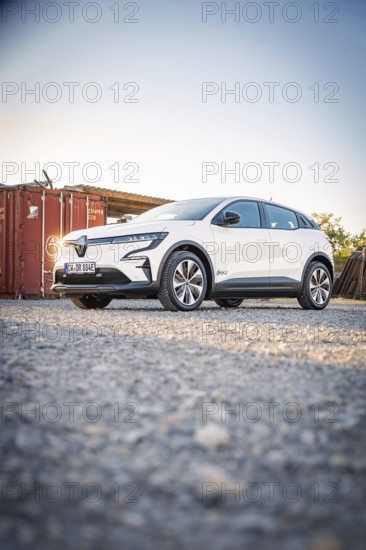 A white electric car stands in front of a container on a gravel field at dusk, Deer E-Carsharing, Renault Megane, Calw, Germany