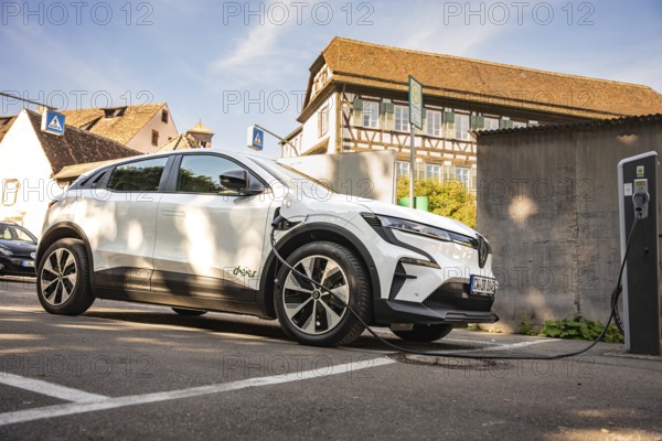 A white electric car charges at a station next to a half-timbered house in a parking lot, Deer E-Carsharing, Renault Megane, Calw, Germany