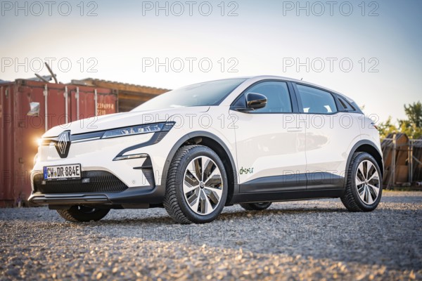 White car on gravel in front of containers in an urban environment with a cloudless sky, Deer E-Carsharing, Renault Megane, Calw, Germany