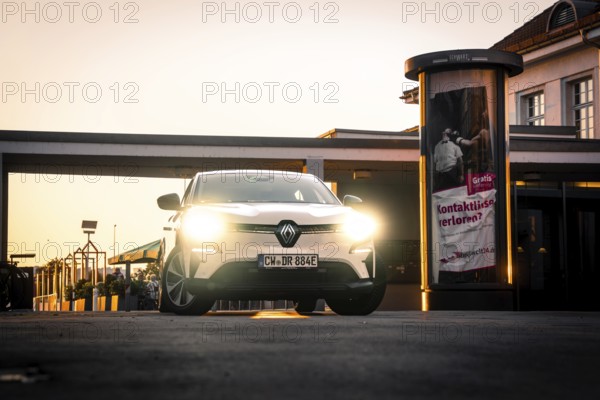 Car with lights switched on stands in front of illuminated lanterns and advertising banners, Deer E-Carsharing, Renault Megane, Calw, Germany
