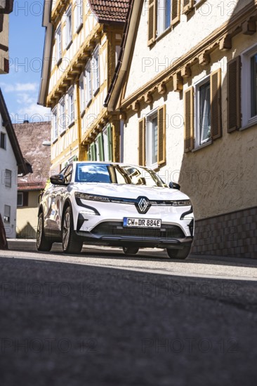 A car drives through a sunlit street in a charming residential area, Deer E-Carsharing, Renault Megane, Calw, Germany