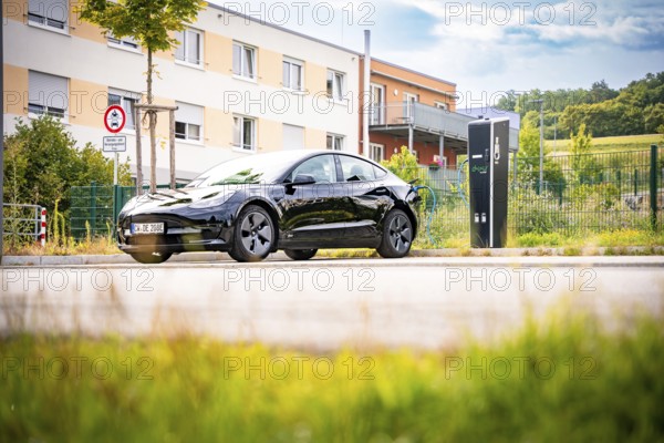 Black car at a charging station in a sunny, urban area, Deer e-Carsharing, Tesla Model 3, Calw, Germany