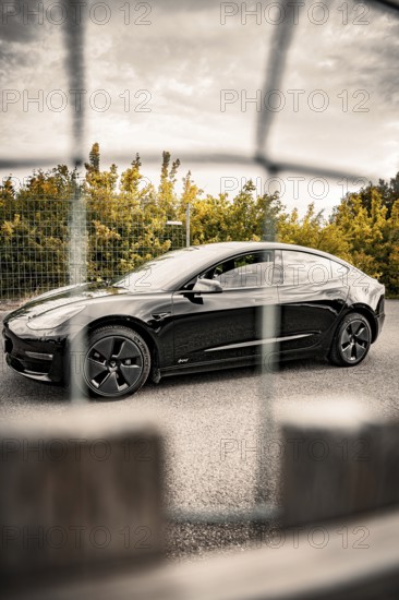 Black car behind a fence on autumnal asphalt, Deer E-Carsharing, Tesla Model 3, Calw, Germany