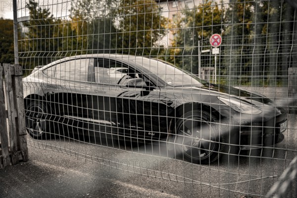 Black car parked at a fence grid in an urban area, Deer E-Carsharing, Tesla Model 3, Calw, Germany