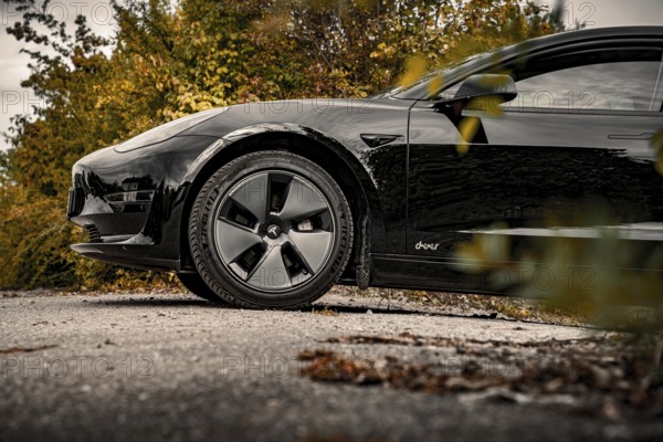 Side view of a black car surrounded by autumn trees and clouds, Deer E-Carsharing, Tesla Model 3, Calw, Germany