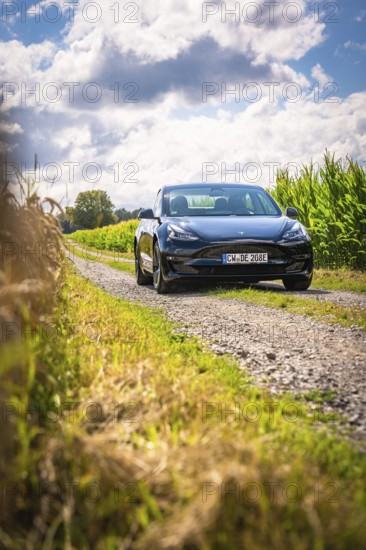 Black car on a narrow road with surrounding fields and clouds, Deer E-Carsharing, Tesla Model 3, Calw, Germany