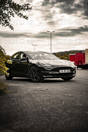 Black car on an empty side of the road surrounded by trees and a cloudy sky, Deer E- car sharing, Tesla Model 3, Calw, Germany