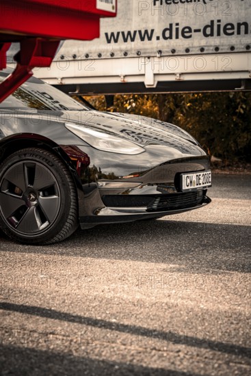 Close-up of a black car with shiny paint and visible reflection on the asphalt, Deer E-Carsharing, Tesla Model 3, Calw, Germany