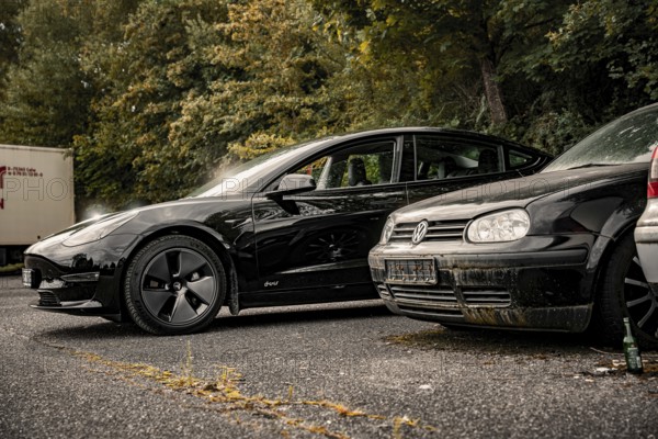 Two black cars side by side in a tree-lined parking lot, Deer e-car sharing, Tesla Model 3, Calw, Germany