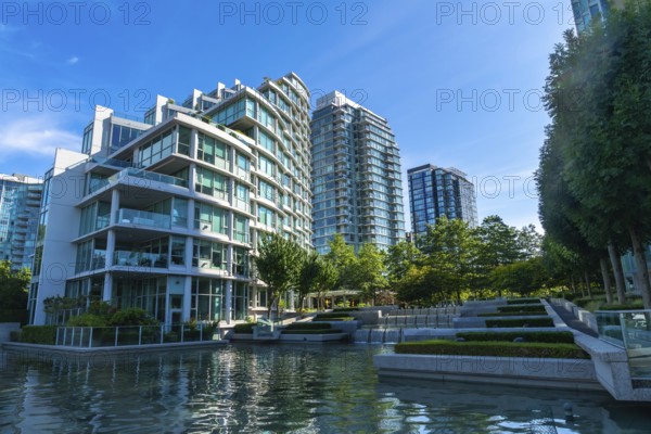 Modern glass and concrete buildings stand tall, reflecting in the calm water of a city park, creating a serene urban oasis in vancouver, british columbia