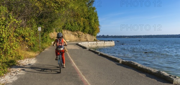 Tourist cycling through stanley park, soaking in stunning ocean views and vibrant cityscapes of vancouver, british columbia, during a sunny summer day filled with adventure
