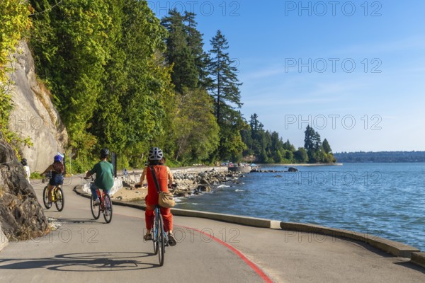 Tourists are cycling on the seawall in stanley park, enjoying the scenic views of the ocean and cityscape on a sunny day in vancouver, british columbia