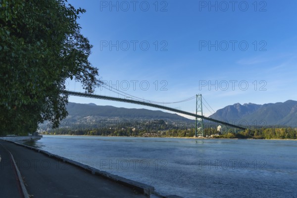 Lions gate bridge spanning burrard inlet, connecting vancouver with stanley park, viewed from the seawall against a backdrop of blue sky and north shore mountains