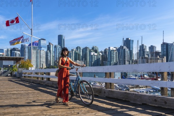 Female tourist walking with her bicycle on a wooden pier, enjoying vancouver downtown skyline in british columbia, canada, on a sunny summer day