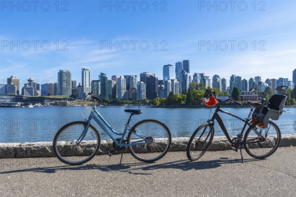 Two bicycles parked along the stanley park seawall overlook vancouver's stunning cityscape, featuring modern towers against a clear blue sky, perfect for cycling and enjoying nature