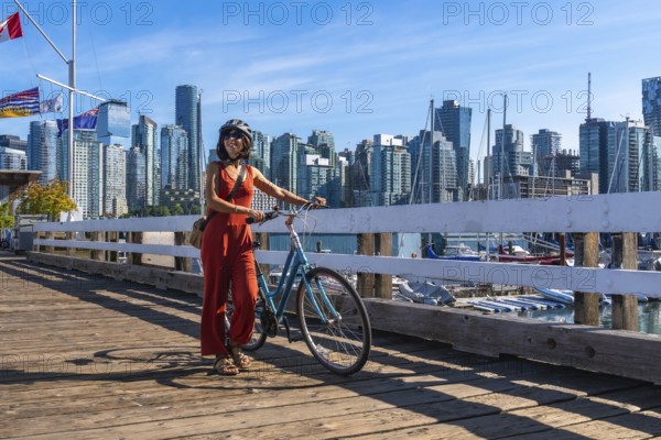 Young woman walking alongside her bicycle on a vibrant pier, soaking in the stunning cityscape of vancouver, british columbia, under a bright blue sky on a sunny day